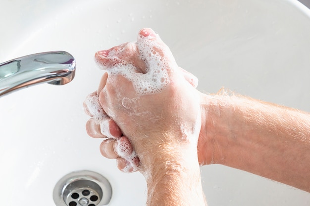 El hombre usa jabón y lavarse las manos debajo del grifo de agua. Concepto de higiene detalle de la mano.