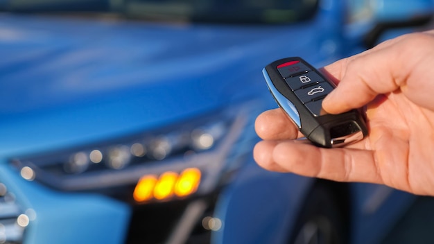 El hombre usa el pulgar para presionar el botón negro en la tecla de control remoto eliminando la señalización de alarma del automóvil azul brillante y los faros parpadean en primer plano