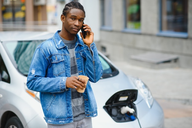 el hombre usa un teléfono inteligente mientras espera y la fuente de alimentación se conecta a los vehículos eléctricos para cargar la batería en el automóvil