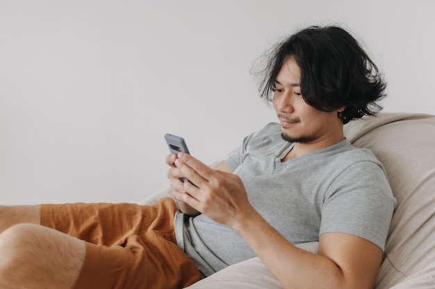 El hombre usa el teléfono inteligente mientras se sienta y se relaja en el sofá de la bolsa de frijoles