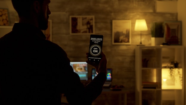 Hombre usando una aplicación de luces inteligentes para encender las luces de la sala de estar. Aplicación y tecnología inteligente