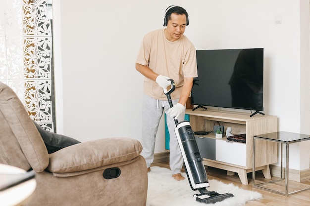 Hombre usando auriculares limpiando alfombras con aspiradora en casa