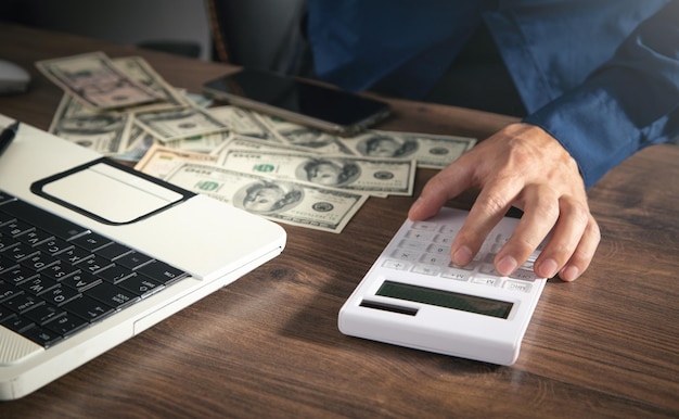 Hombre usando calculadora con dinero y computadora en la mesa