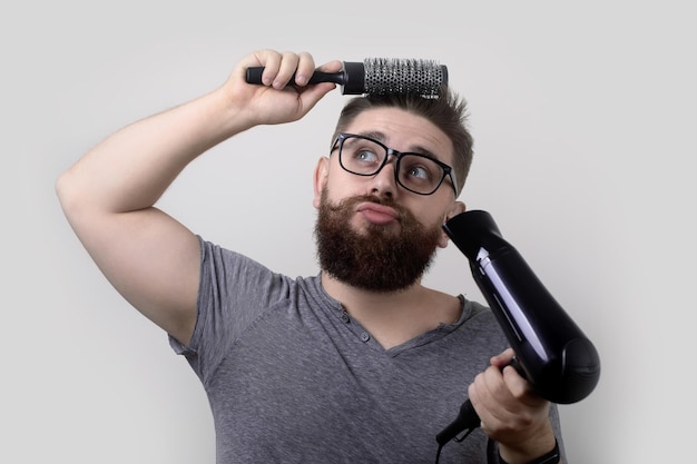 El hombre está usando cepillo de pelo y secador de pelo para su peinado  sobre fondo gris, concepto de hombres estilista | Foto Premium