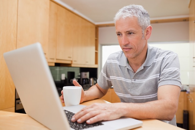 Hombre usando una computadora portátil mientras bebe café