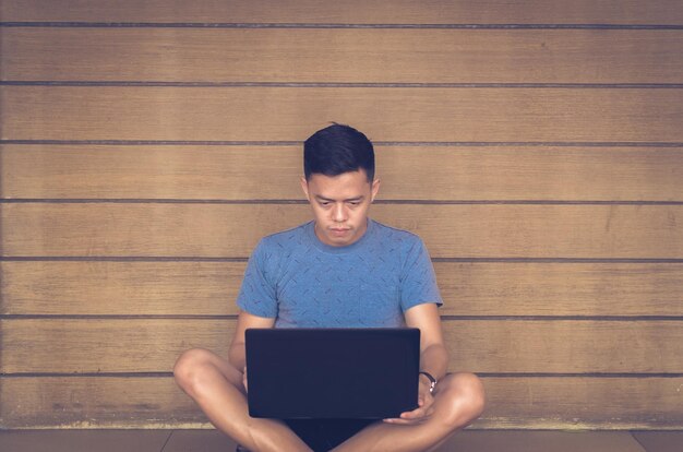 Hombre usando una computadora portátil mientras está sentado contra la pared