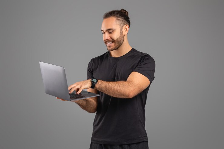 Hombre usando una computadora portátil y sonriendo en un fondo gris