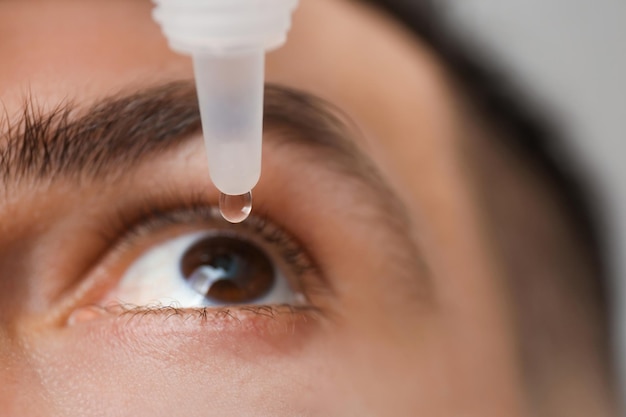 Hombre usando gotas para los ojos en primer plano de fondo gris