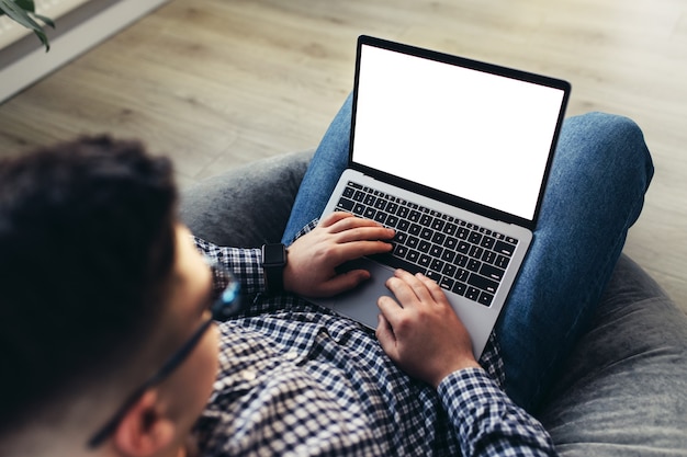 Hombre usando laptop, con gafas, muebles acolchados. Fondo borroso