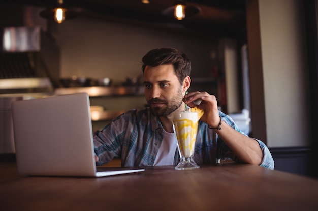 Hombre usando laptop mientras toma batido