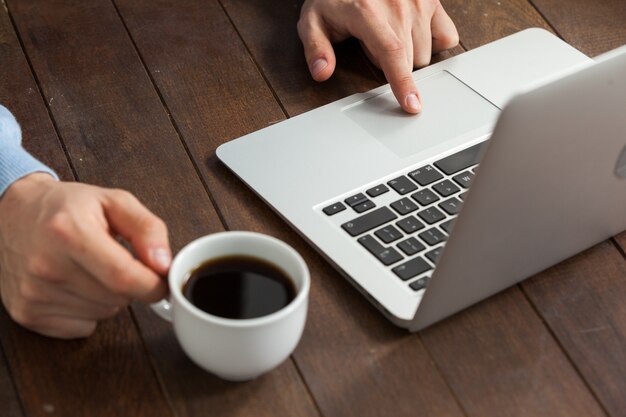 Hombre usando laptop mientras tomando una taza de café