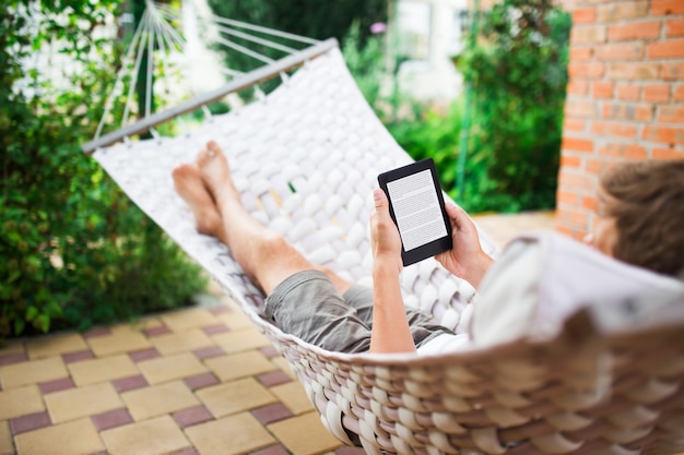 Hombre usando un libro electrónico con texto de lorem ipsum en la pantalla mientras se relaja en una hamaca