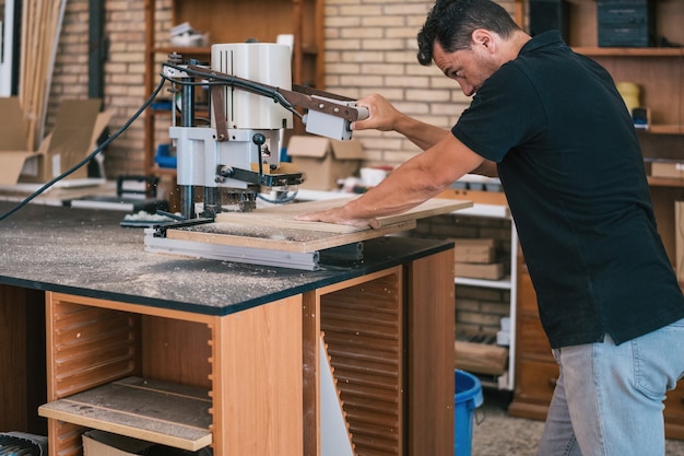 Hombre usando una máquina eléctrica para cortar un panel de madera en un taller