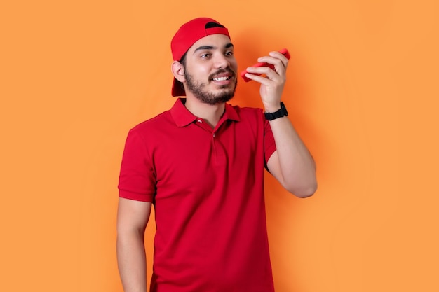 Hombre usando el reconocimiento de voz del teléfono posando aislado sobre fondo naranja en el estudio