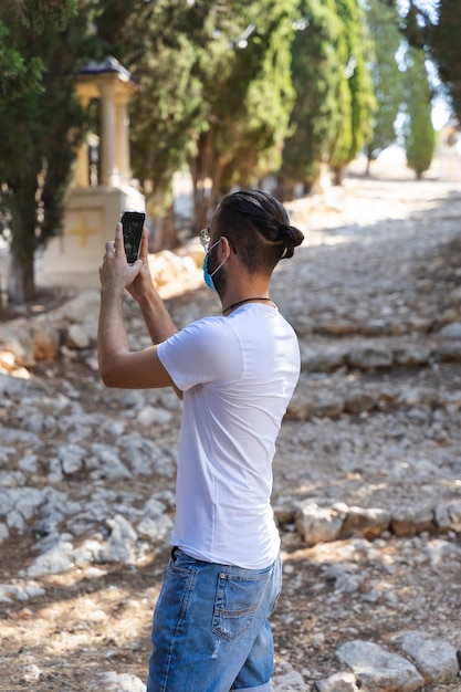 Hombre usando su teléfono móvil para tomar una foto con una máscara y una camiseta blanca