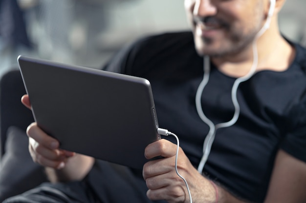 Hombre usando una tableta digital y auriculares mientras está sentado en un sofá