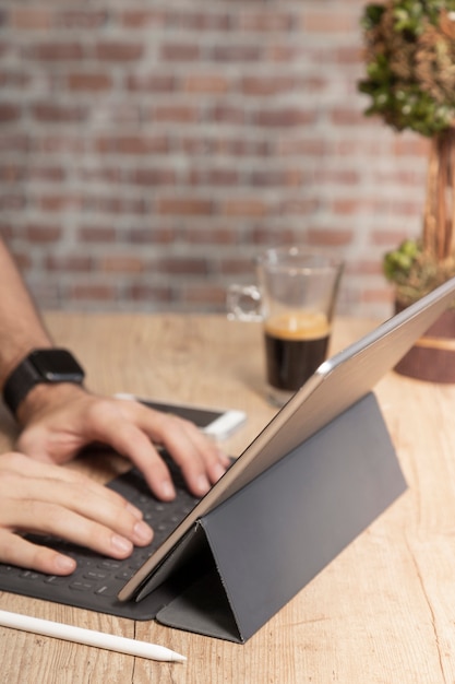 Hombre usando una tableta para trabajar, en una mesa de madera con una taza de café, frente a una pared de ladrillos