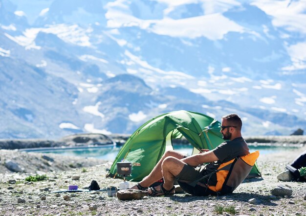 Hombre usando un teléfono inteligente cerca de una tienda en las montañas