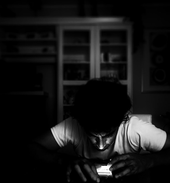 Foto hombre usando teléfono inteligente mientras está sentado en la mesa en el cuarto oscuro