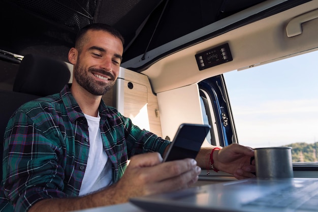 Hombre usando teléfono móvil y computadora portátil desde su caravana