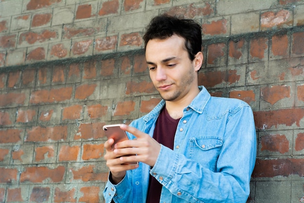 Foto hombre usando teléfono móvil contra una pared de ladrillo