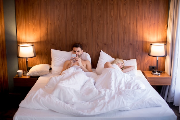 Hombre usando teléfono móvil mientras esposa durmiendo en la cama