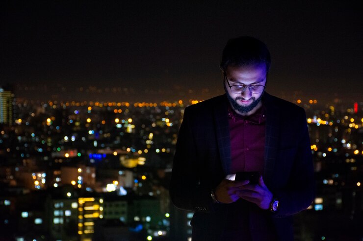 Foto hombre usando teléfono móvil mientras está de pie contra la ciudad iluminada por la noche