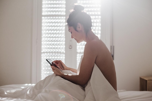 Hombre usando teléfono móvil mientras está sentado en la cama en casa