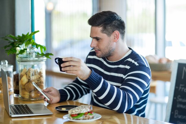 Hombre usando un teléfono móvil mientras toma una taza de café