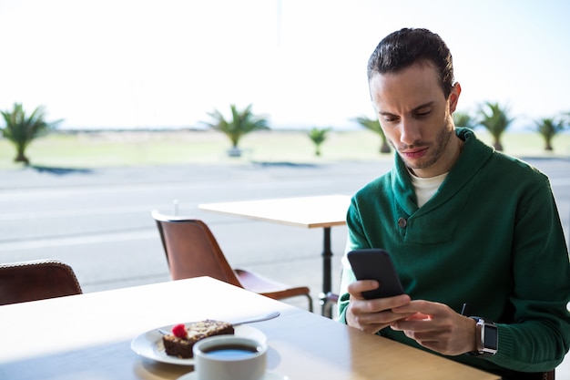 Hombre usando un teléfono móvil con pastel y una taza de café en la mesa