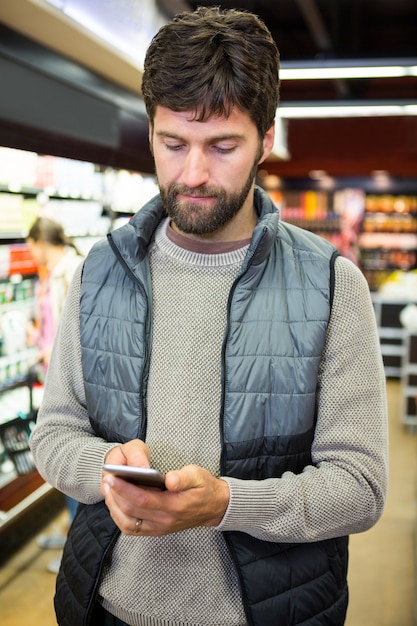 Hombre usando un teléfono móvil en la sección de comestibles mientras compra