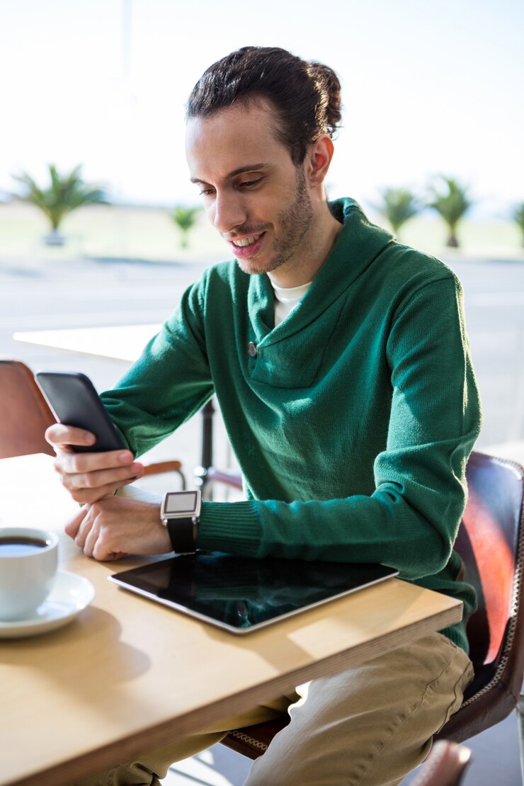 Foto hombre usando un teléfono móvil con tableta digital y una taza de café en la mesa