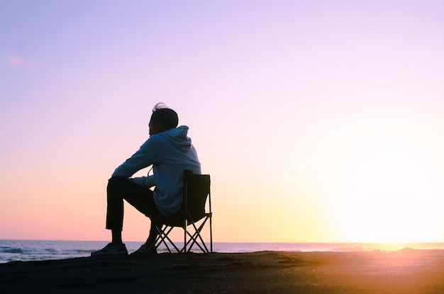 Un hombre de vacaciones se relaja en una tumbona en una playa tropical durante el colorido atardecer