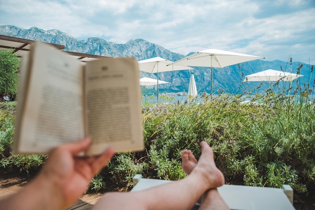 Hombre de vacaciones de verano acostado en una tumbona leyendo un libro con una hermosa vista