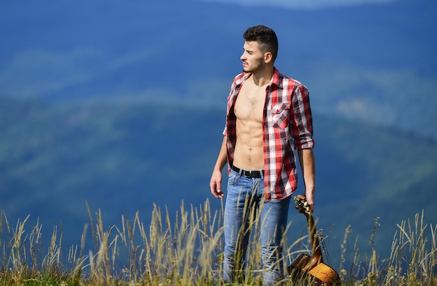 Hombre vaquero de calor de roca pura con torso musculoso desnudo guitarrista acústico canción de música country hombre sexy con guitarra en camisa a cuadros moda hipster camping occidental y senderismo feliz y libre