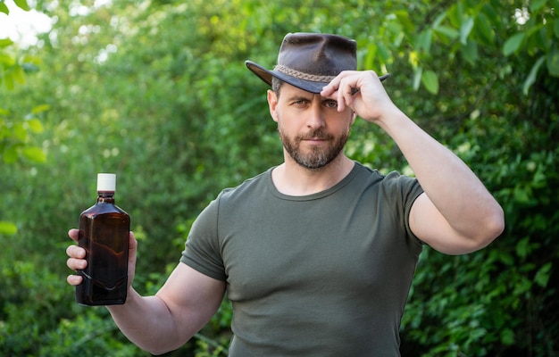 Hombre vaquero ofreciendo whisky Hombre vaquero con botella de whisky Hombre vaquero con whisky al aire libre