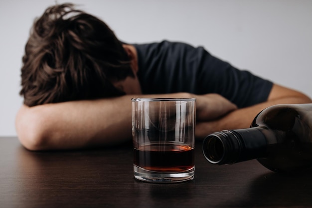 Hombre con vaso y botella de whisky acostado o durmiendo en la mesa Alcoholismo y adicción