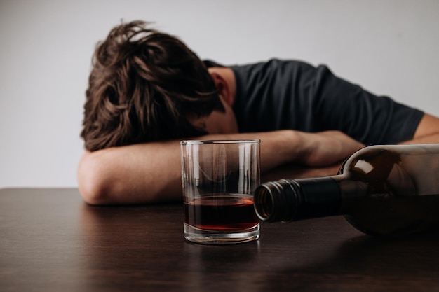 Hombre con vaso de whisky y botella vacía sobre una mesa Concepto de adicción