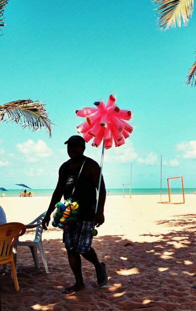 Foto hombre vendiendo juguetes en la playa contra el cielo