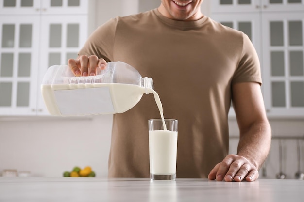 Hombre vertiendo leche de una botella de un galón en un vaso en una mesa de mármol blanco en el primer plano de la cocina
