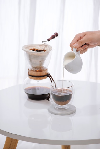 Foto hombre vertiendo leche en vaso con café frío en la mesa