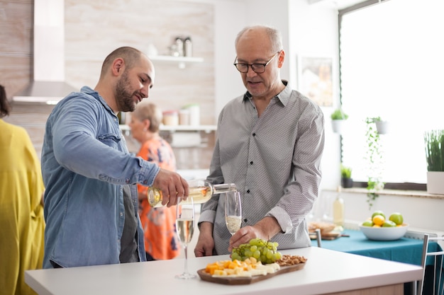 Hombre vertiendo vino a su padre en la cocina durante el almuerzo familiar.