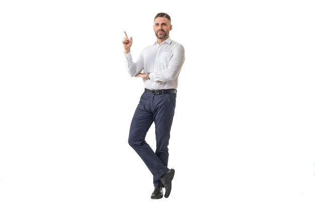 Un hombre vestido con una camisa blanca y pantalones negros posa con confianza apuntando hacia arriba con el dedo