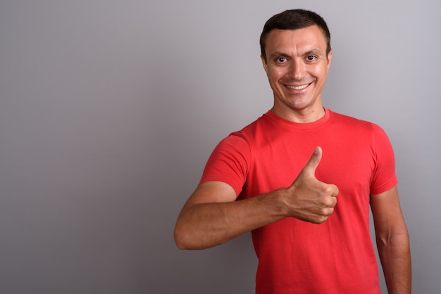 Hombre vestido con camisa roja contra la pared gris