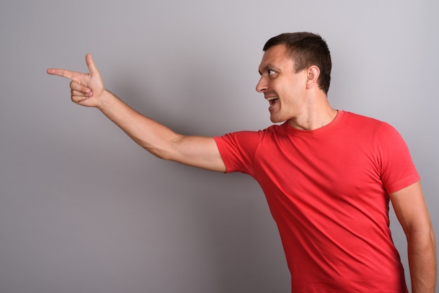 Hombre vestido con camisa roja contra la pared gris