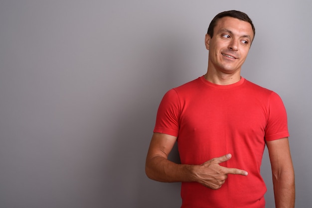 Hombre vestido con camisa roja contra la pared gris