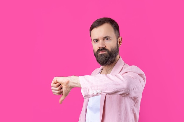 Un hombre vestido con una chaqueta rosa con barba muestra un pulgar hacia abajo.