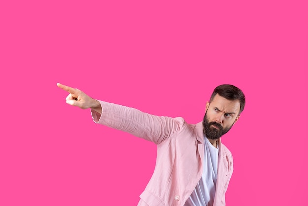 Un hombre vestido con una chaqueta rosa indica la dirección en un fondo rosa aislado