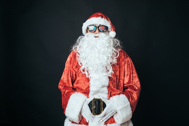 Hombre vestido como Santa Claus con gafas con letra de configuración de tv, sobre fondo negro. Concepto de Navidad, Santa Claus, regalos, celebración.