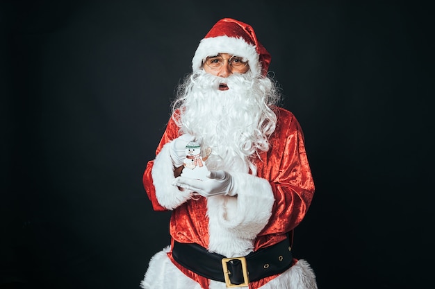 Hombre vestido como Santa Claus sosteniendo un pequeño muñeco de nieve, sobre fondo negro. Concepto de Navidad, Santa Claus, regalos, celebración.